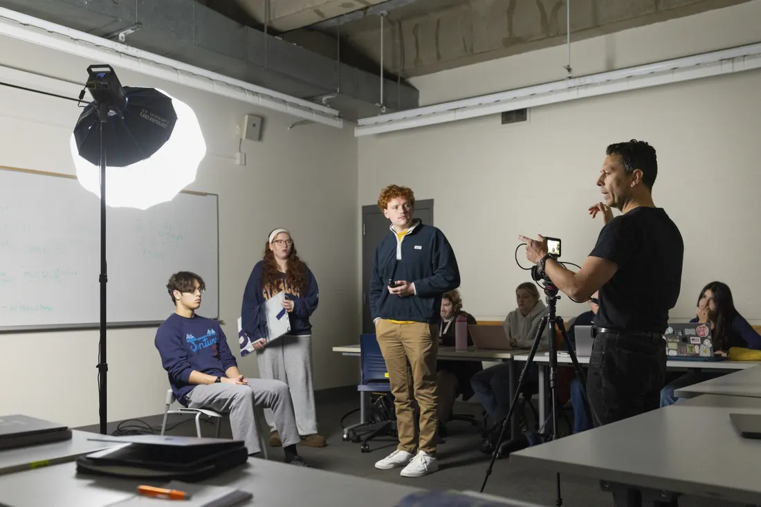 Person standing in front of a camera in a studio directing other people.