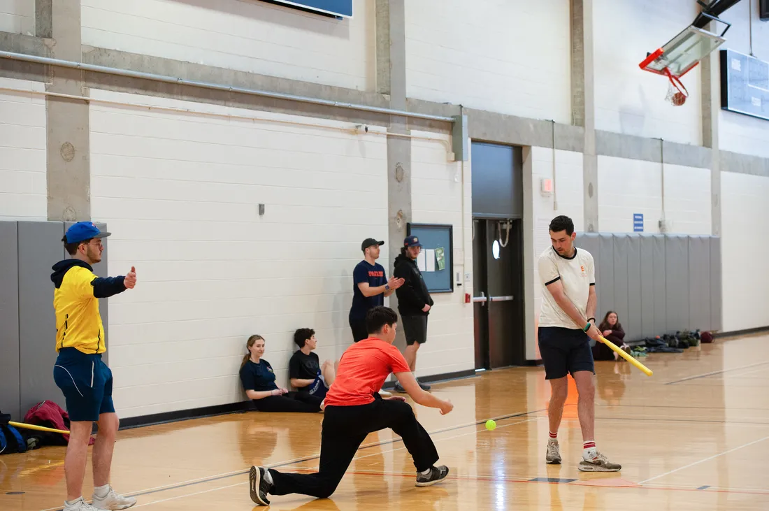 Students playing wiffleball in the gym.