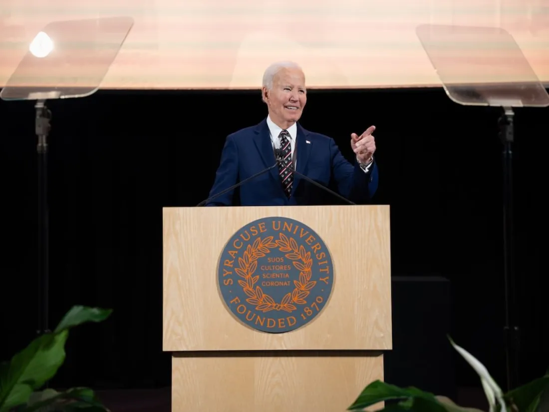 President Joe Biden at a podium speaking at Syracuse University during his portrait unveiling ceremony.