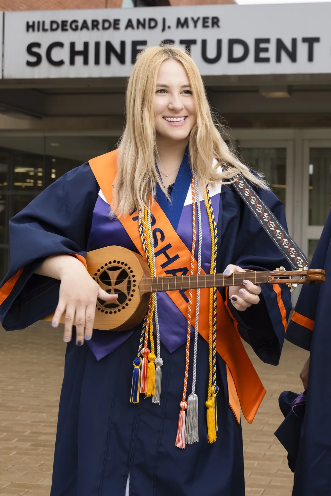 Anna Meehan '26 in her graduation regalia smiling and playing a small, stringed instrument.