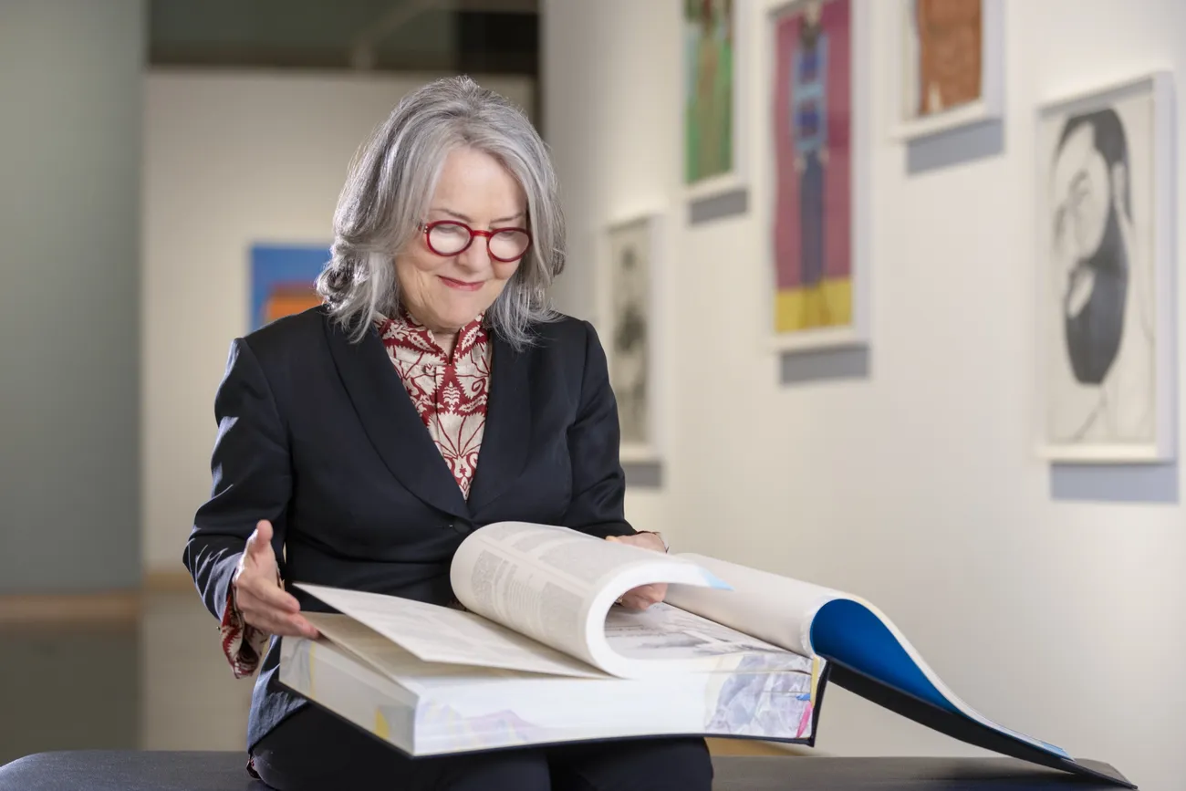 Diana Wege '76 flipping the pages of a large book.
