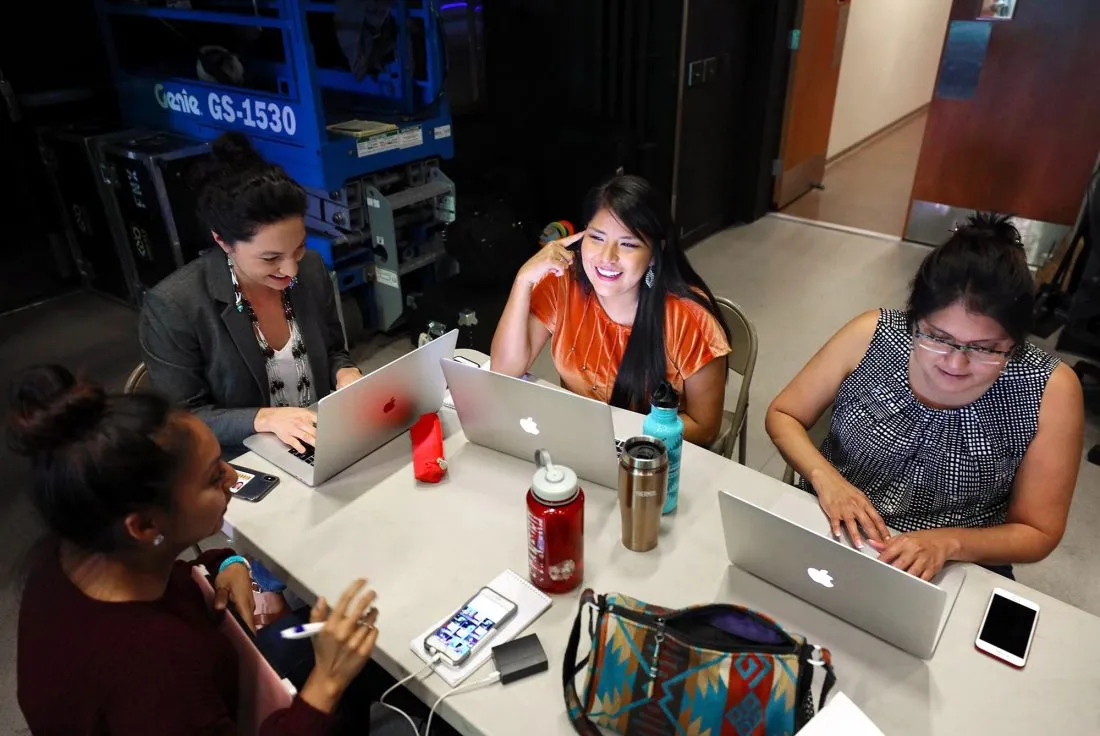 Four women sit around a table in a newsroom reviewing the election updates