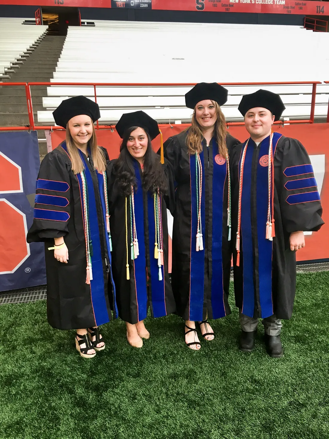Alumna Katie Verderber in her graduation regalia standing alongside fellow Syracuse University alumni on their graduation day.