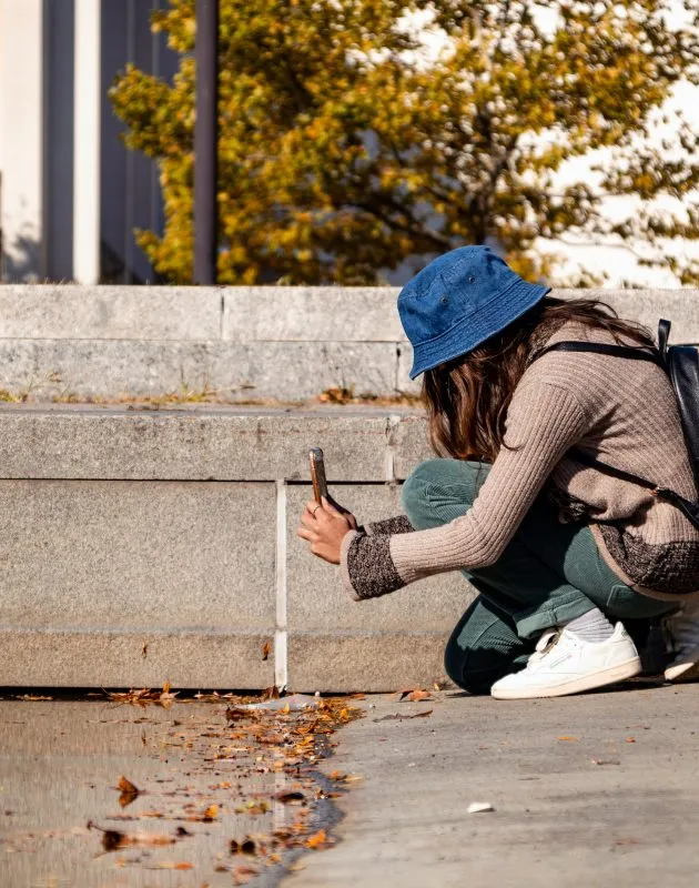 Person kneels down to photograph a cement wall with a smart phone.