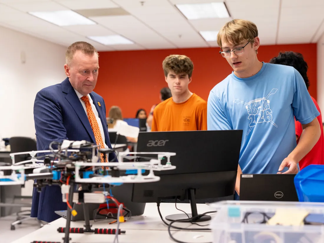 Chancellor Mike Haynie standing with two students observing a drone.