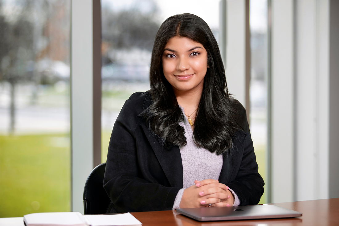 Portrait of Zainab Kumandan, smiling with her hands clasped on a table.