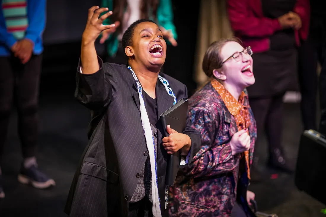 Danielle Coles and Becky Leifman on stage, mouths open wide in performance.