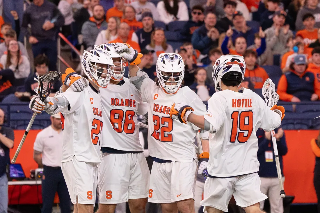 Members of the Syracuse University men's lacrosse team celebrating on the field in the JMA Wireless Dome.