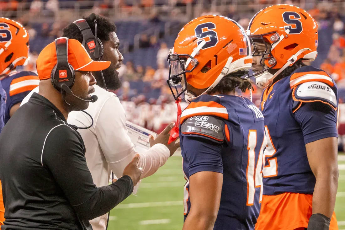 Person with headset on speaking to Syracuse University football players.