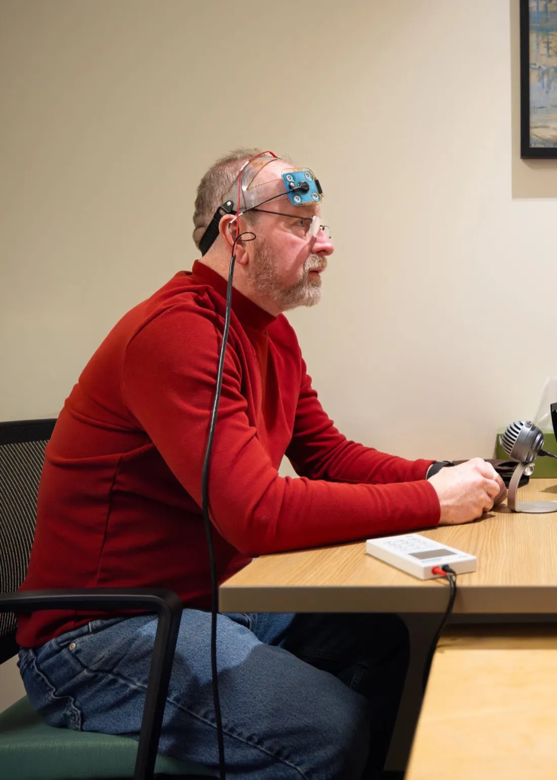 Stroke aphasia patient sitting down with a transcranial direct current stimulation device on his head.
