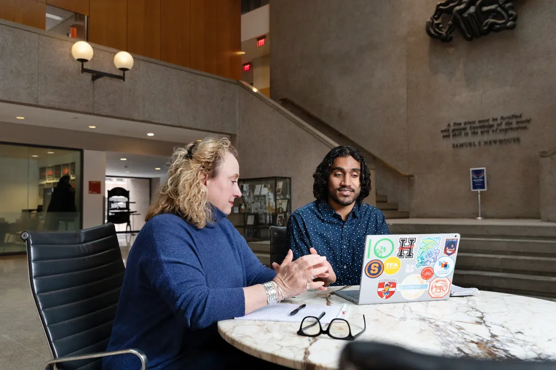 Melissa Chessher and Gaurav Shetty sitting at a table looking at an open laptop.