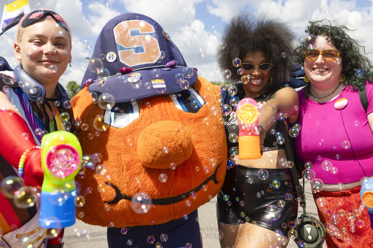Syracuse University affiliated people playing with bubbles at the CNY Pride Parade with Otto the Orange.