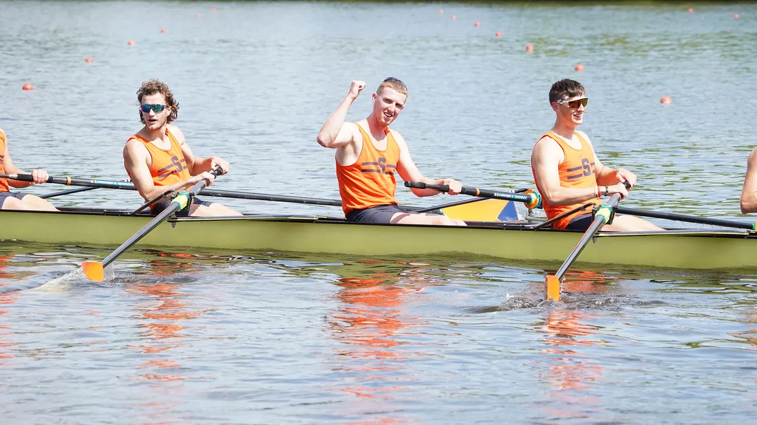 Closeup of rowing team on the water with team member pumping fist in air.
