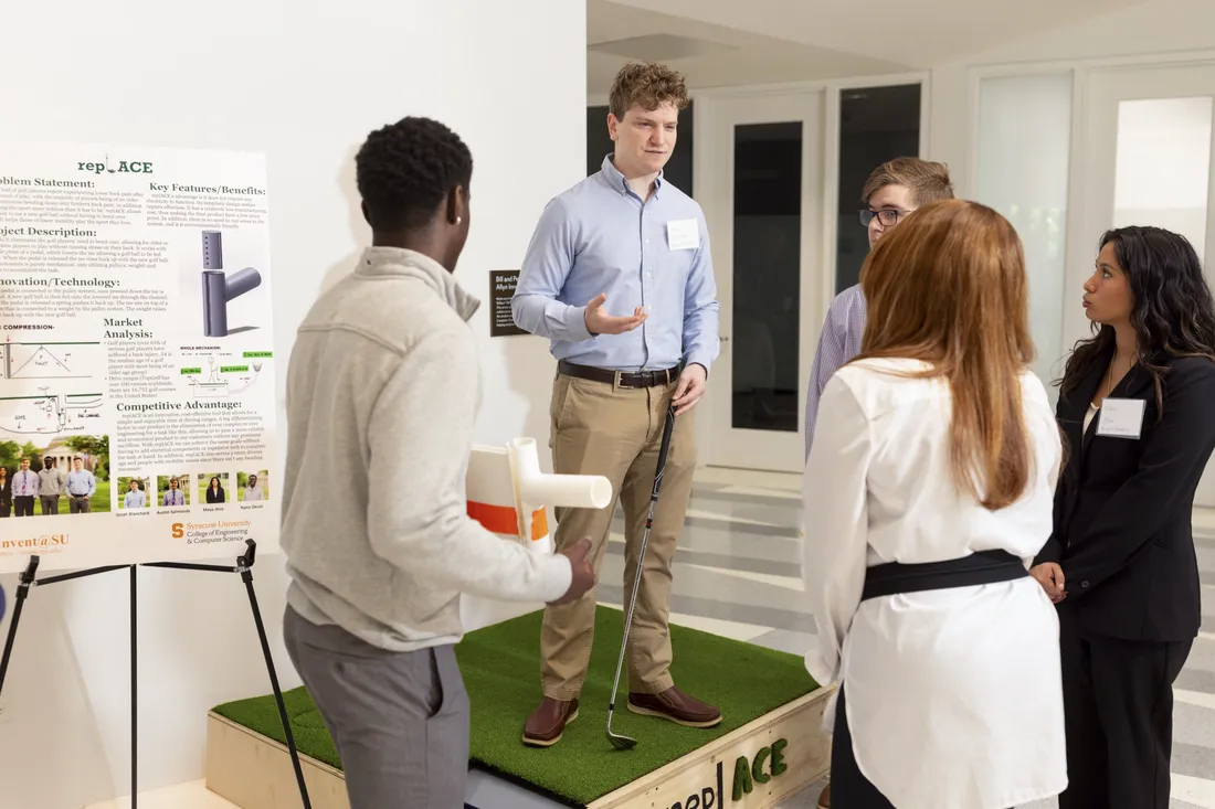 Student standing on a platform presenting their pitch to a group at the Invent@SU event.