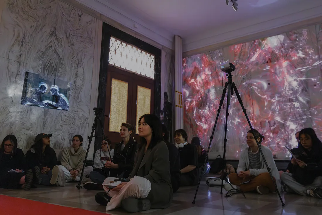 Ngai Lan Tan sits in room surrounded by peers in exhibition.