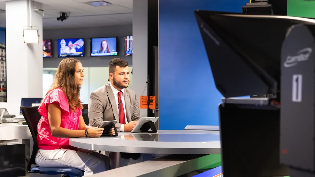 Students sitting at a television news desk.