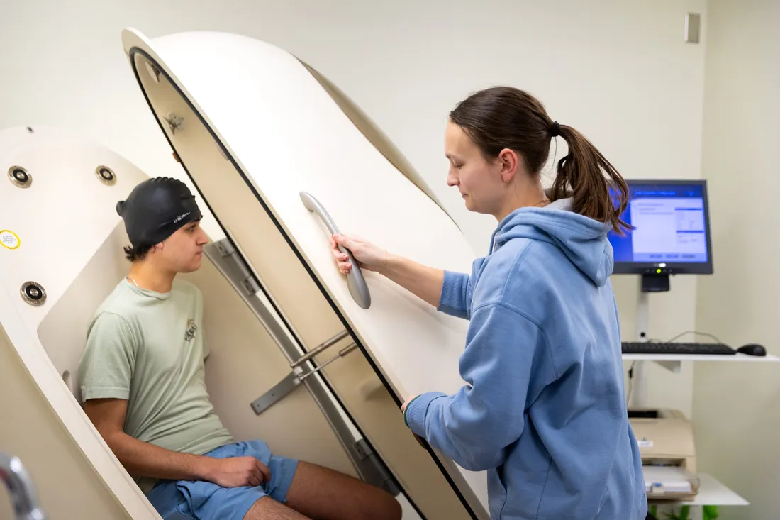 Student sitting inside of a "Bod Pod", a large device that measures hydration levels.