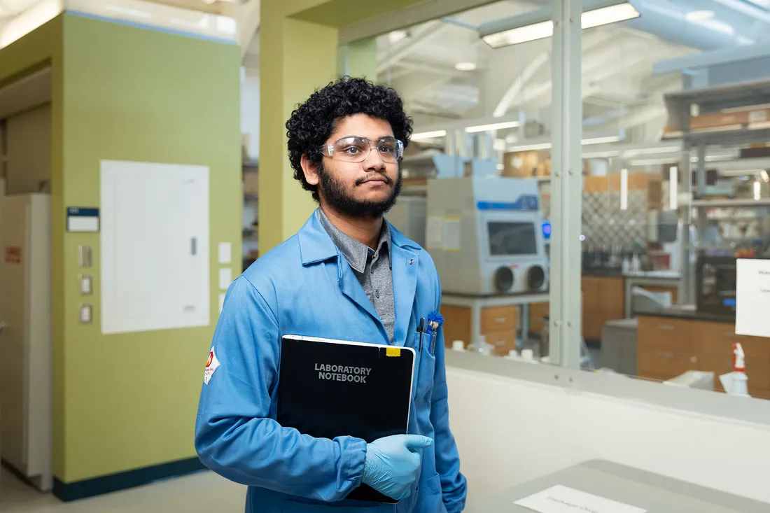Student posing with a binder in front of a lab.