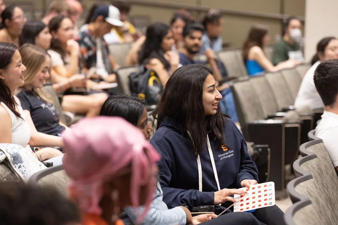 Laughing students sit together in auditorium holding bingo cards.