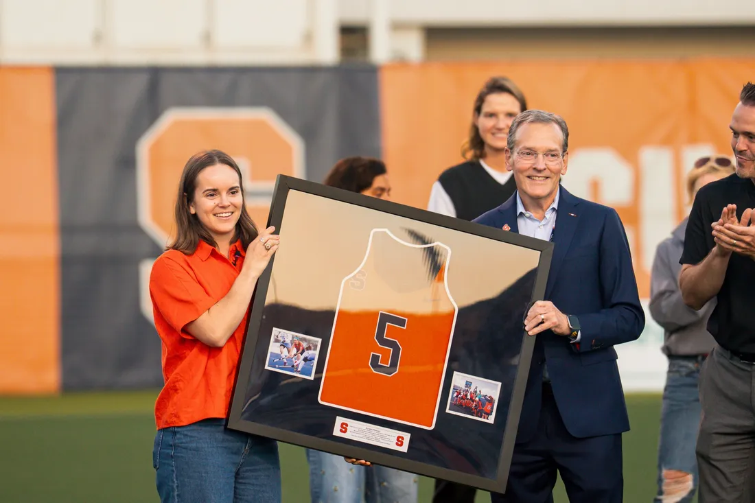 Two people standing and holding a framed sports jersey.