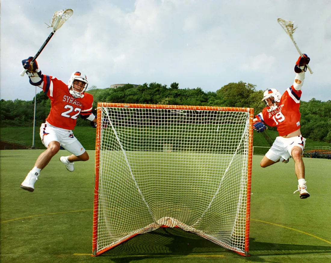 Gary Gait and his brother jumping next to a lacrosse net.