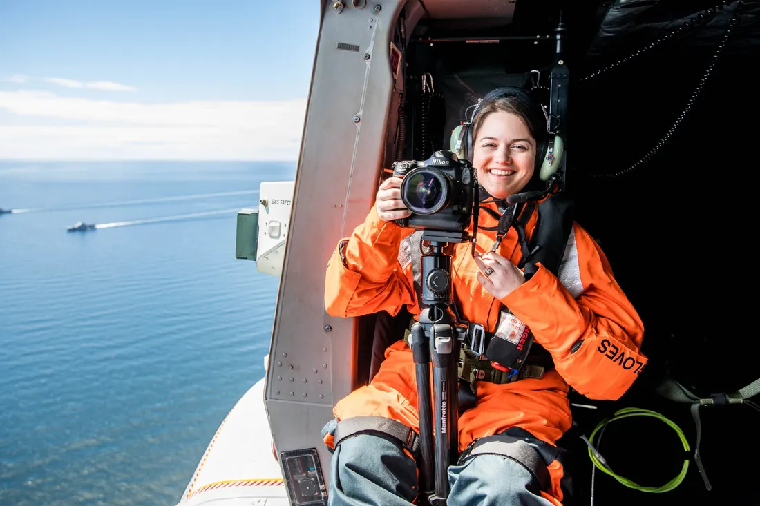 Portrait of Shannon Smith '21 sitting at an open door of a plane in the sky, with a camera, smiling.