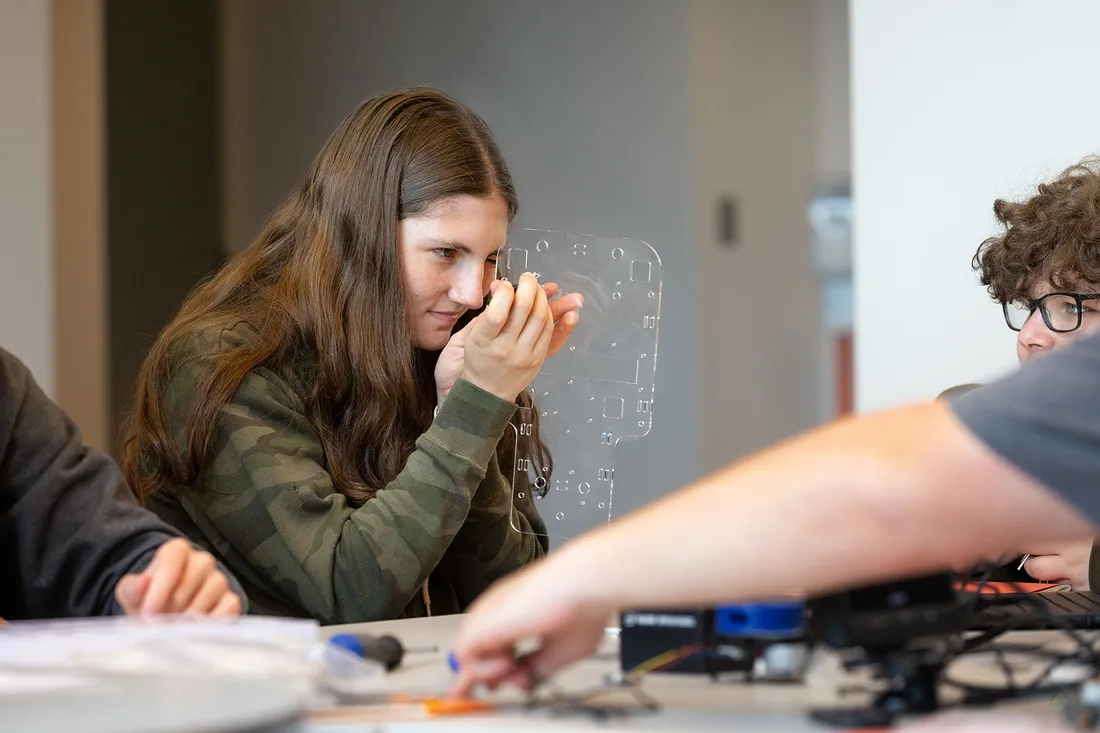 Student peers closely at mechanical part in workshop.