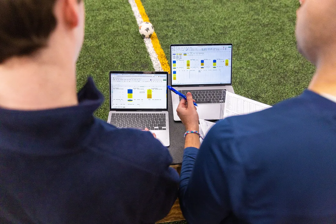 Two students looking at computers on a soccer field.