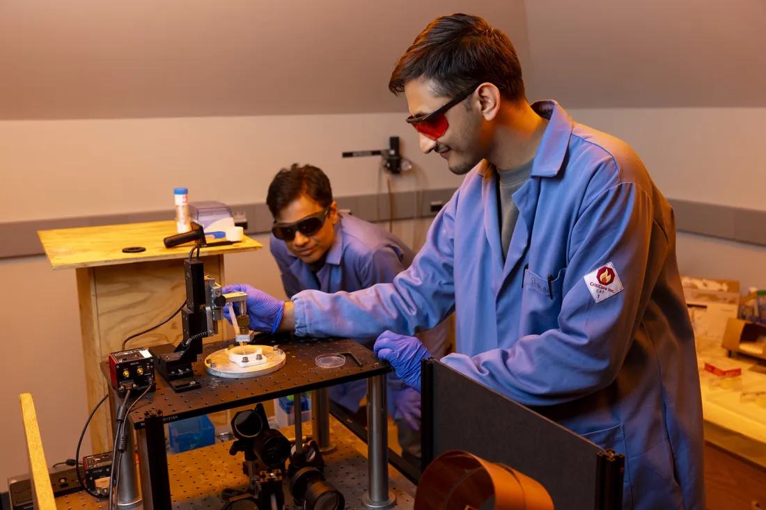 Pranav Soman watching Sharad Timilsina work with an optics printer in a laboratory.