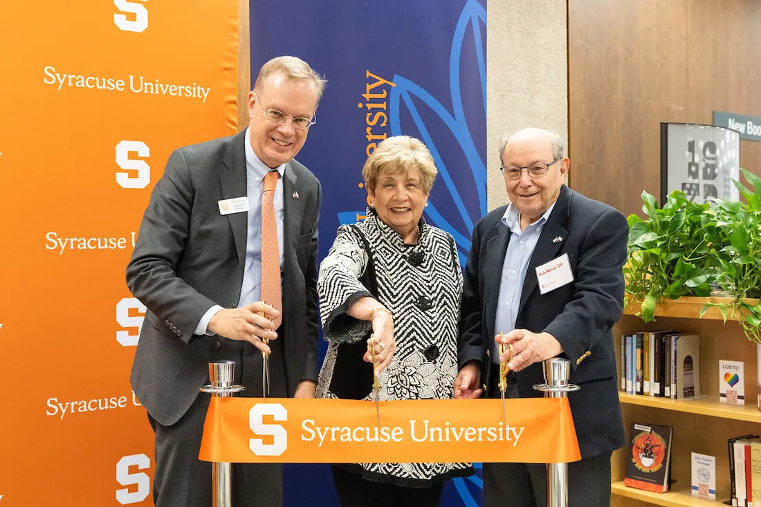 Three people cutting a ribbon during a ceremony at a library on campus.