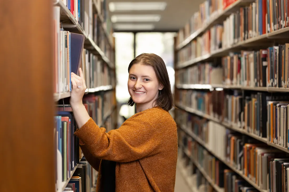 Student inside of library choosing book from shelf.