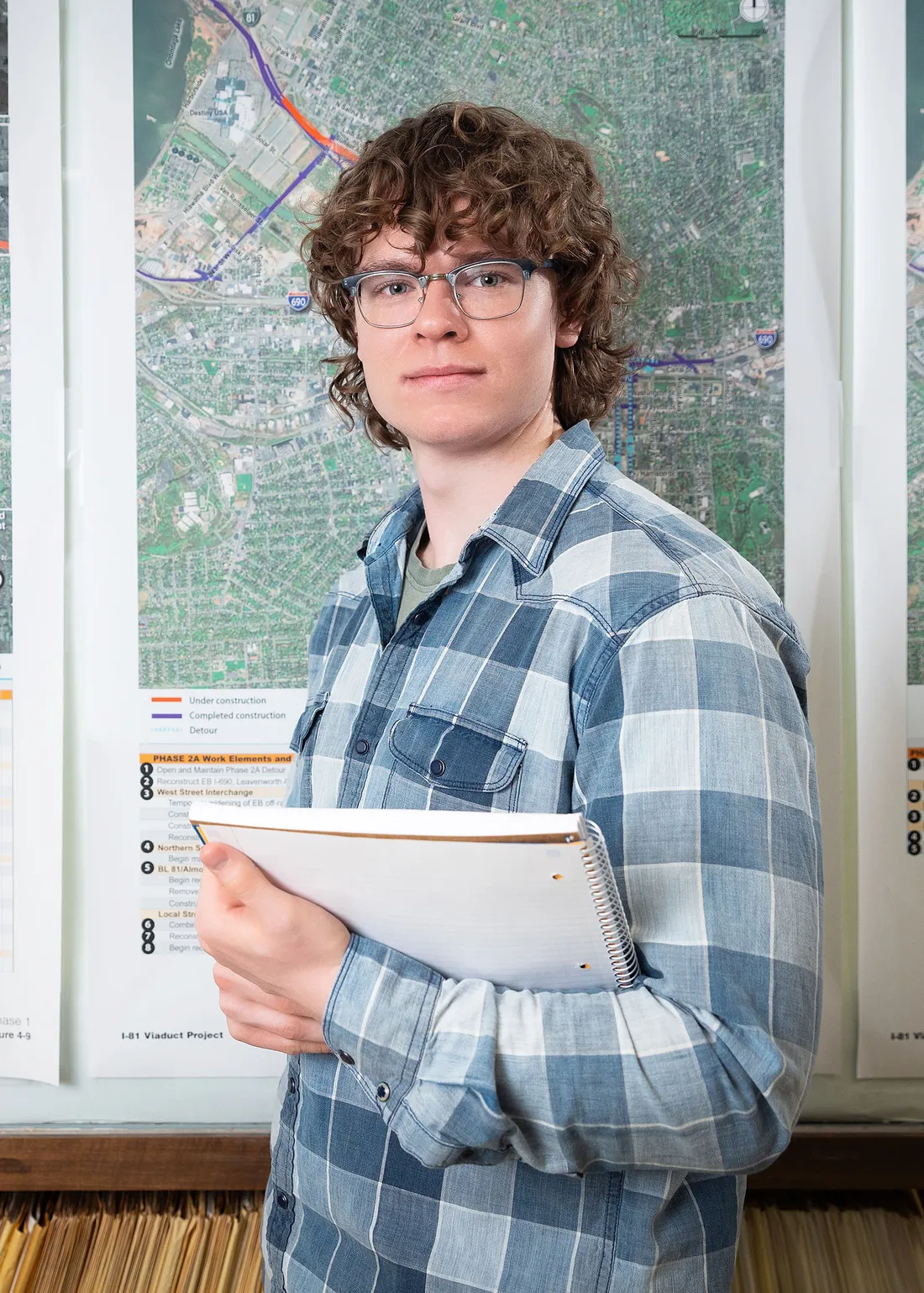 William Burke standing in front of a map holding a note book.