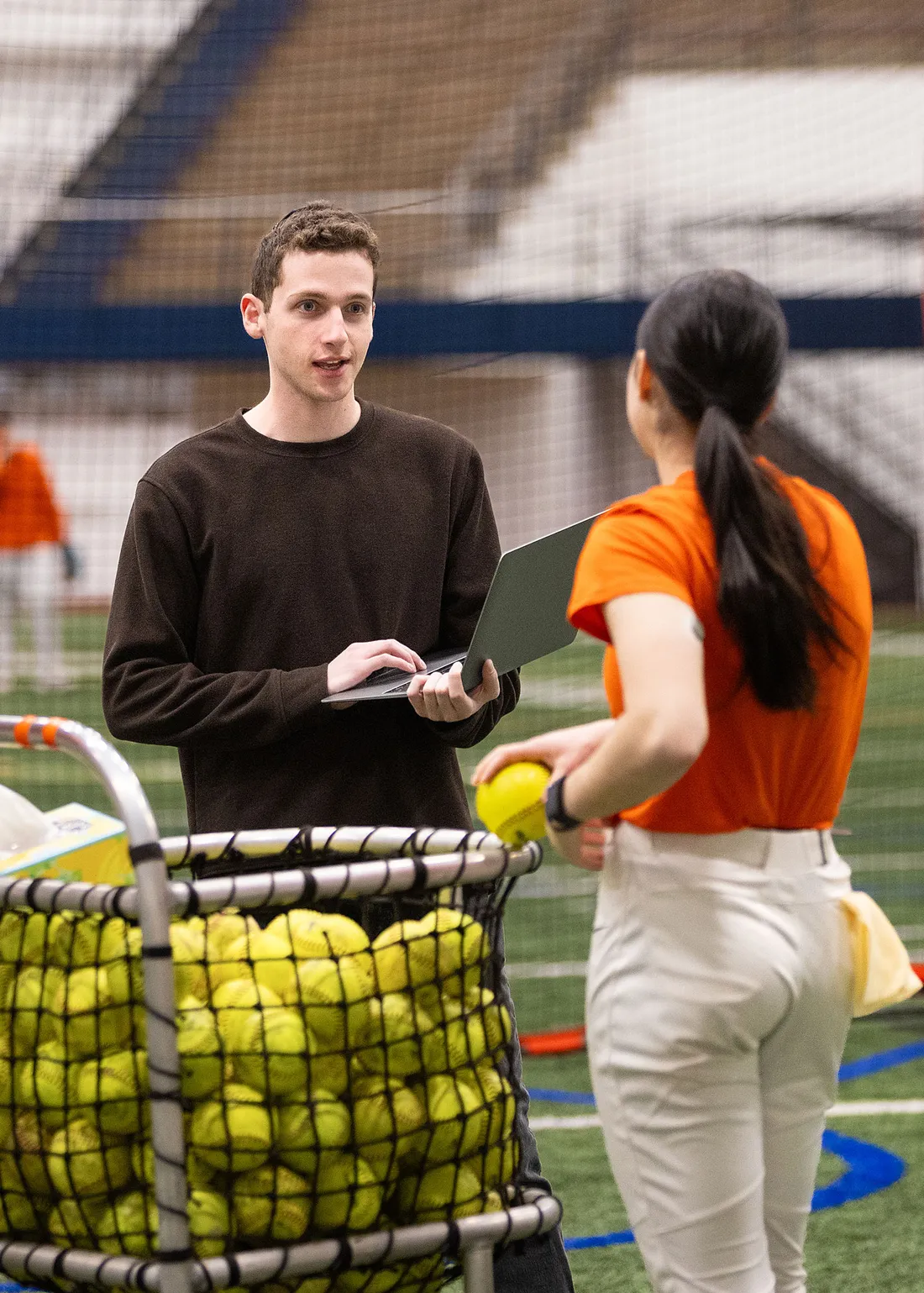 Gavi Sela is talking to a softball player while on a computer.